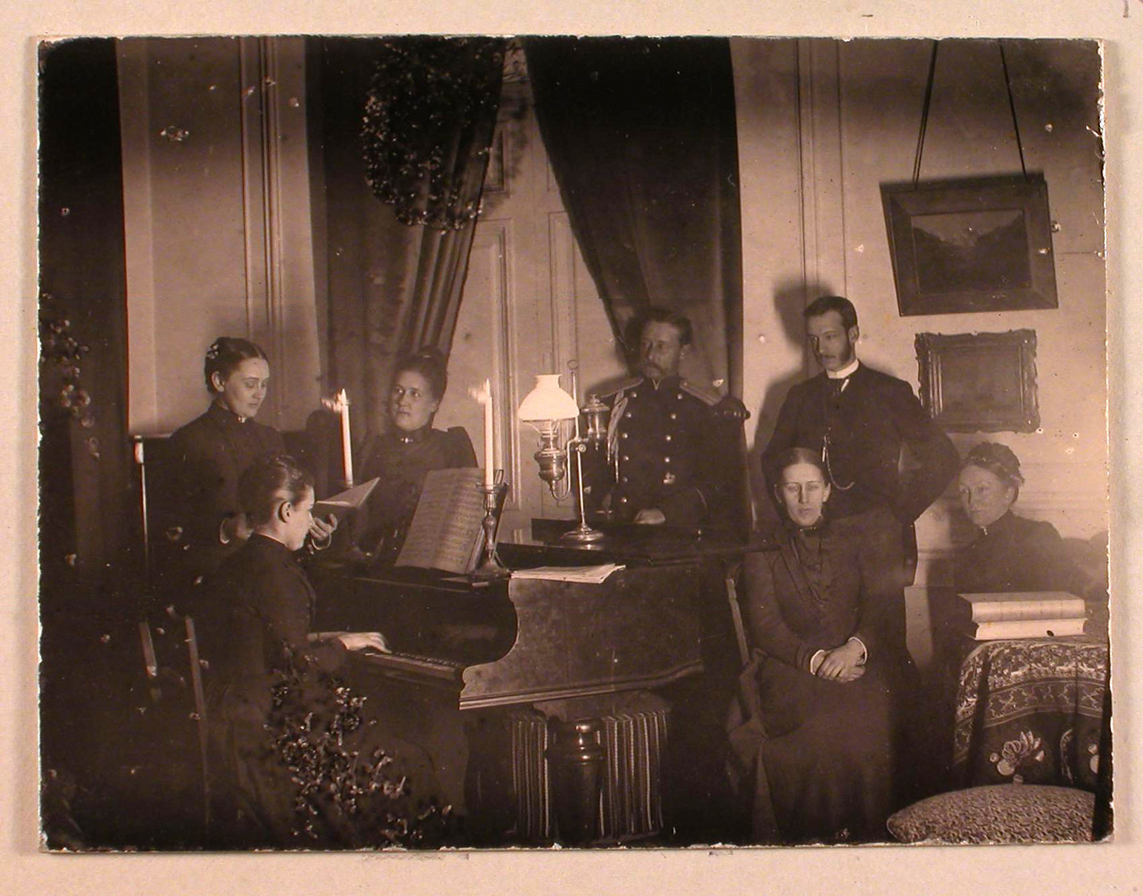 61. Члены семьи Николаи-Пален в гостиной усадебного дома: за роялем Софья Николаевна фон дер Пален (урожд. Николаи), рядом с ней - Мария Николаевна Николаи; в группе справа стоит Павел Николаевич (Пауль Эрнст Георг) Николаи, перед ним сидит Александра Николаевна Николаи; крайняя справа Софья Егоровна Николаи (урожд. Мейендорф). 1890-е