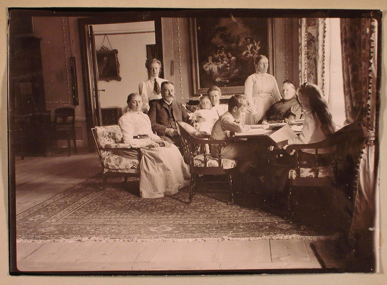 66. Семья Николаи-Пален в гостиной; слева направо: Мария Николаевна Николаи, граф Константин Константинович Пален, за ним стоит его старшая дочь Маргарита, Софья Николаевна фон дер Пален (урожд. Николаи) с дочерью Еленой на руках, Александра Николаевна Николаи (стоит), Софья Егоровна Николаи (урожд. Мейендорф); за столом - дети Паленов Николас и Софья